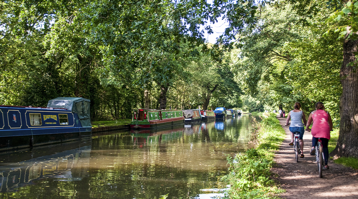 Des bateaux étroits sont amarrés sur la Rivière Wey Navigation et des personnes font du vélo sur le chemin de halage, Surrey, Angleterre
